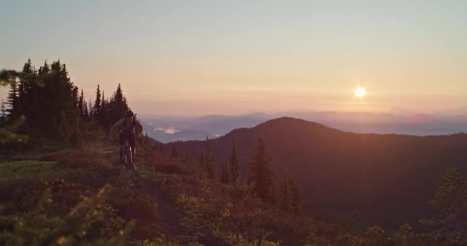 A man mountain biking on an exposed alpine ridge trail against the setting sun