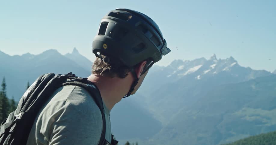 A man wearing a bike helmet looks off at the mountain range in the distance