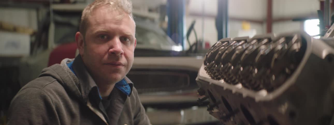 An mechanic is sitting near a vehicle engine