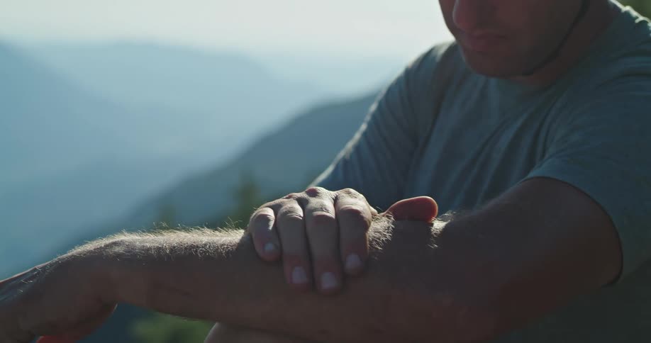 A man sitting on an exposed mountainside slaps a mosquito