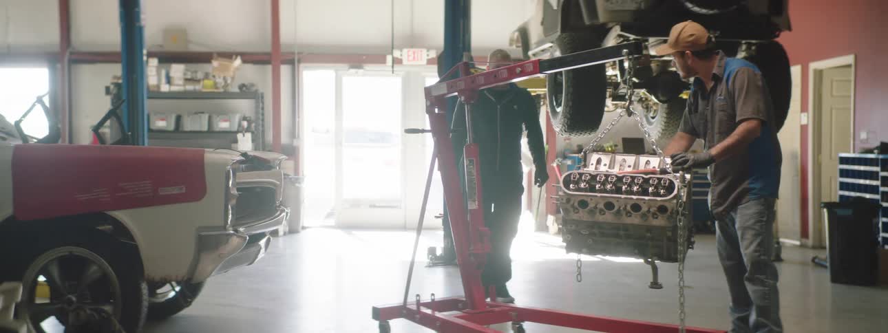 Two mechanics crouch down to examine a transmission in an auto garage