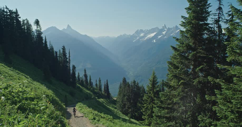 A person rides a bicycle up out of a valley on a mountainside trail