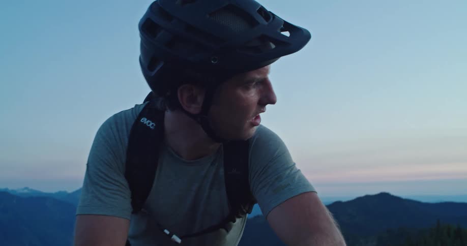 A mountain biker catches his breath while resting on his bike high in the mountains at dusk