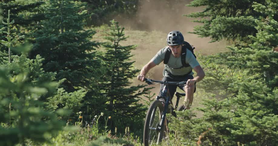 A man with a helmet riding a cross country bicycle in a forest with trees