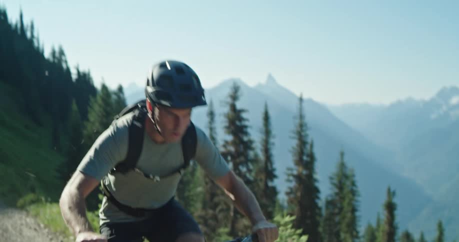 A man with a helmet riding a mountain bike with a mountain range and clear sky behind him