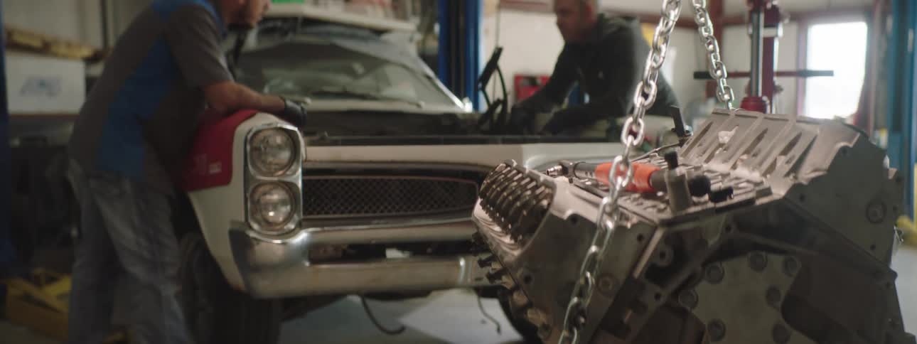 Two men that are working on an engine in a vehicle in a shop