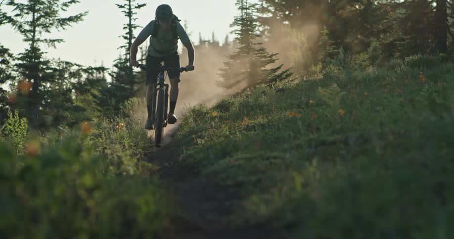 A person rides a bike on a dusty meadow trail at sunset
