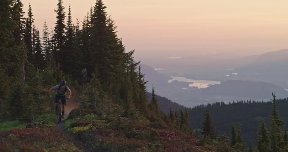 Someone on a bicycle is vigorously riding up a forest mountain trail high above the valley