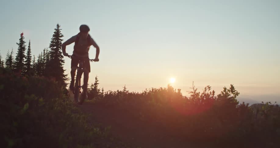 A mountain biker pedals hard along an exposed ridge trail with the sun setting behind them