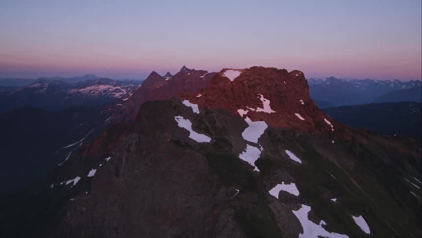 A rocky mountain top covered in patches of snow in last light from the sun
