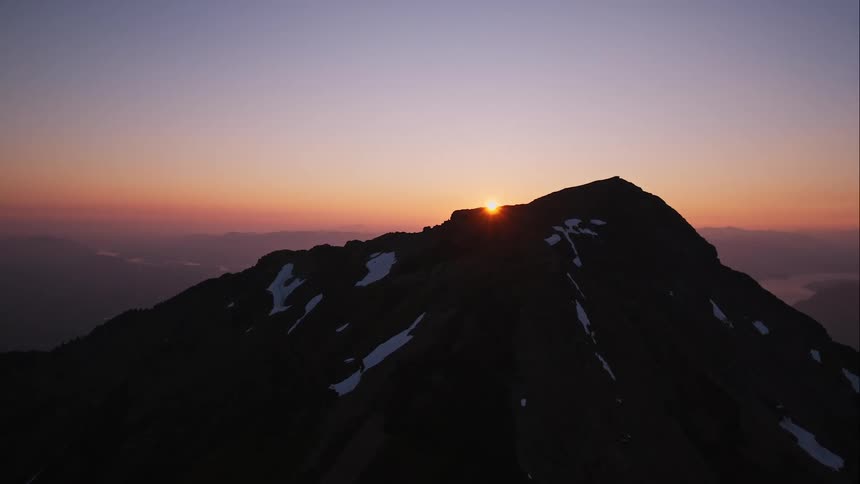Aerial view of rugged mountain revealing setting sun and pink skies