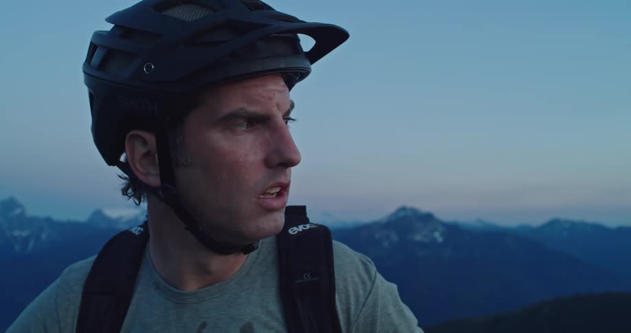 A man with a helmet stands on top of a mountain range and looks around
