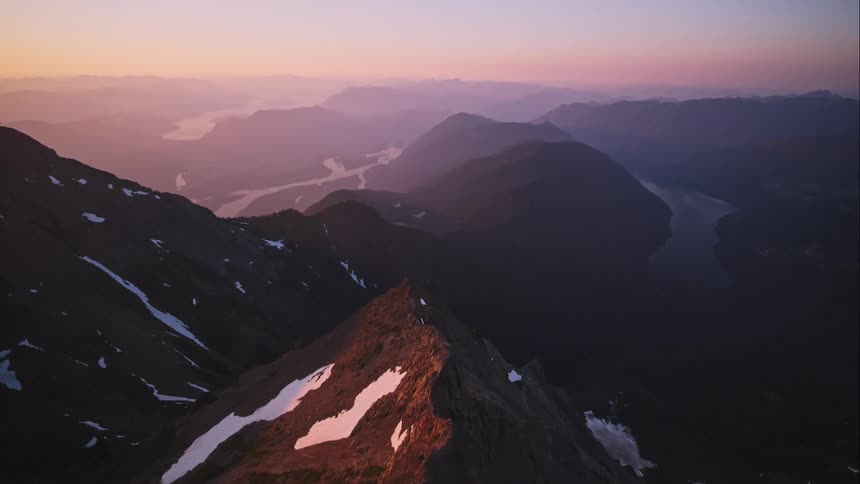 Aerial shot of a mountain peak with lakes and rivers seen below