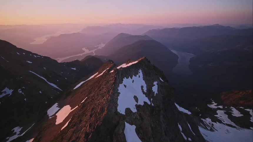 Aerial view of mountain ridge at sunset revealing lakes and distant summits