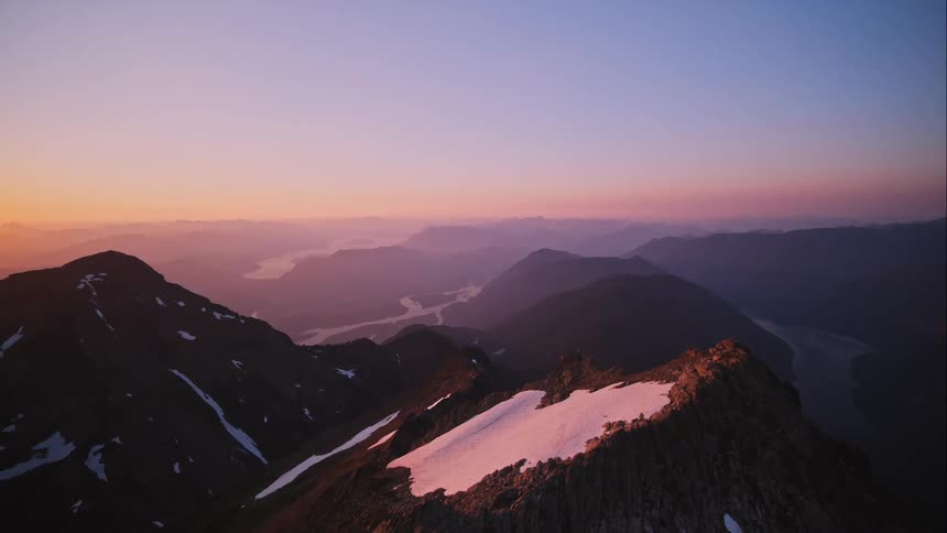 Mountain peaks high in a colorful sky and a sunset on the horizon