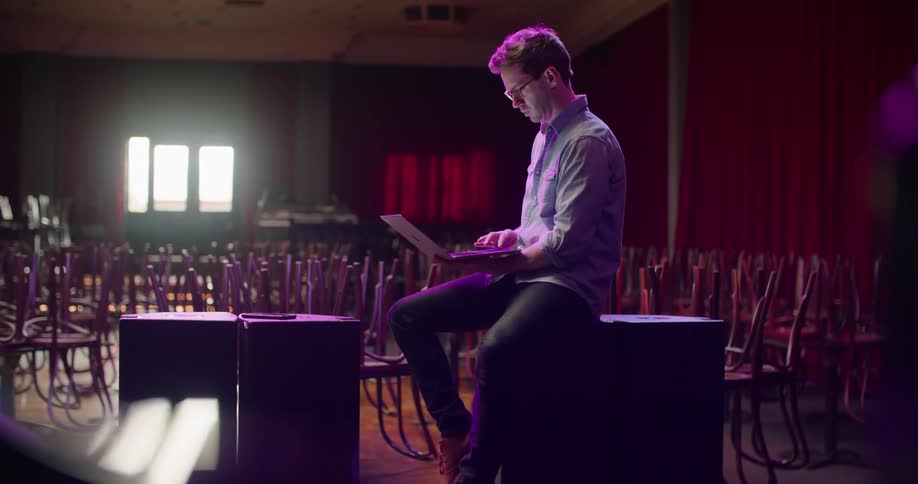 A man in a nightclub using a laptop with chairs and tables in the background