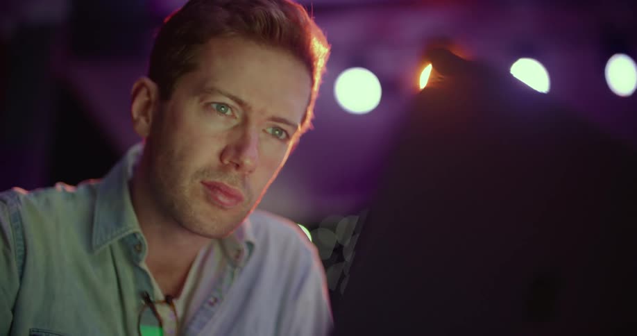 Man looks at a laptop with bright lights shining behind him