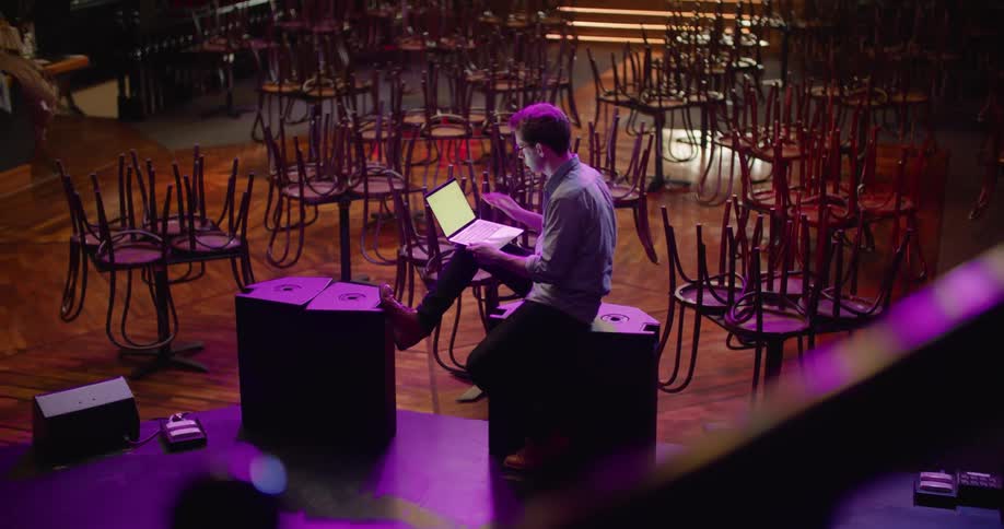 A man sits and picks up his laptop while in an empty nightclub
