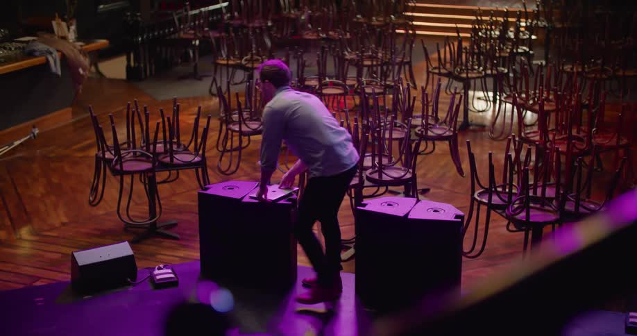 A man closes his laptop and sets it down before jogging off of the stage at an empty night club