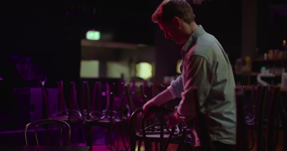 A man is putting tables and chairs together in a venue