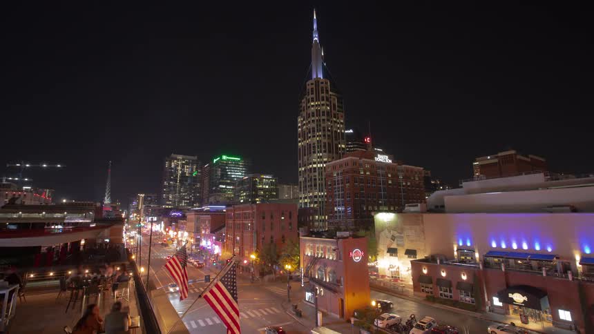People sit on a rooftop as cars travel down the street in the city at night