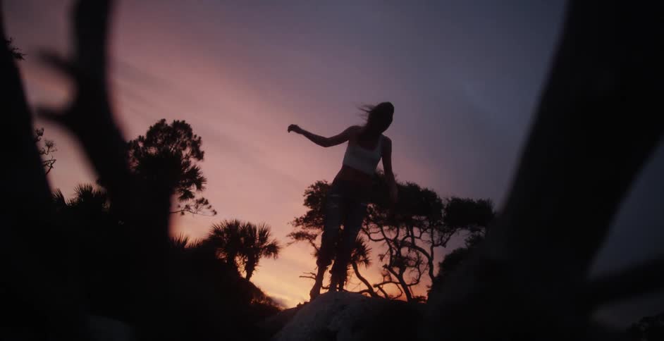 A woman balances on stones as the sunsets