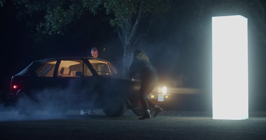 A woman running into a car next to a man and a glowing pillared with a tree in the background