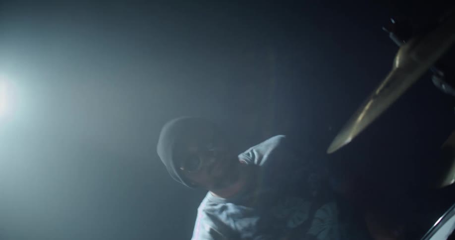 A man is playing the drums on the dark stage