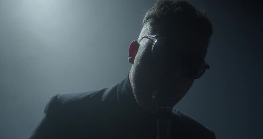 Man wearing glasses sings into a microphone
