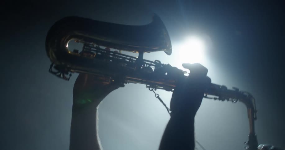 A man in a room playing a saxophone with a spotlight and a wall in the background