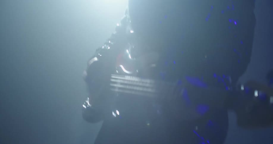 Guitarist with beard plays guitar on foggy stage under spotlight