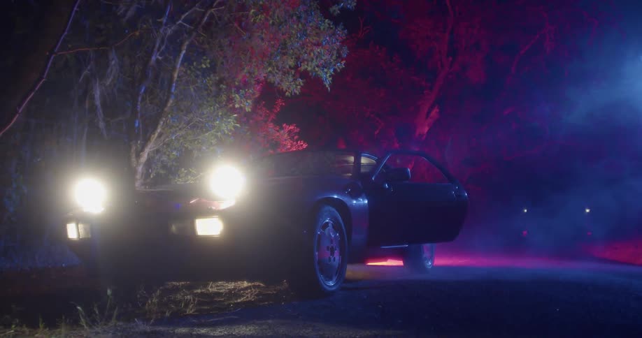 A vehicle with headlights and its door open on the side of her road with trees in the background