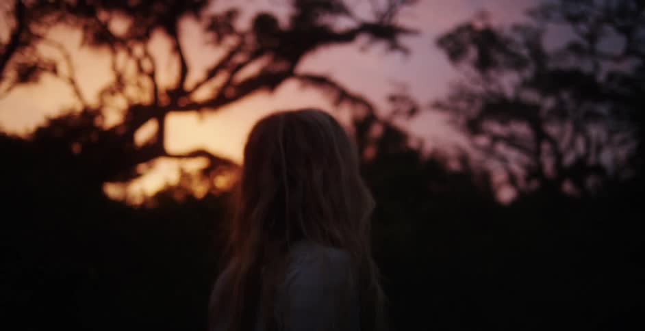 A blond woman walks through a forest at sunset