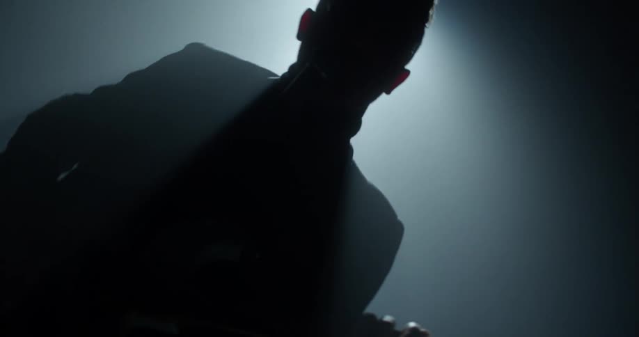 The camera spins away from a guitarist who is illuminated by a single spotlight