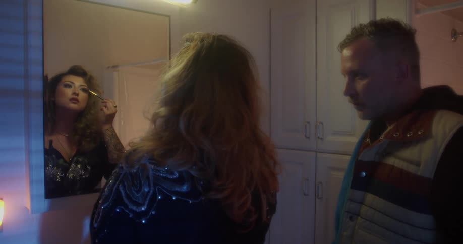 A man is watching a woman put on makeup