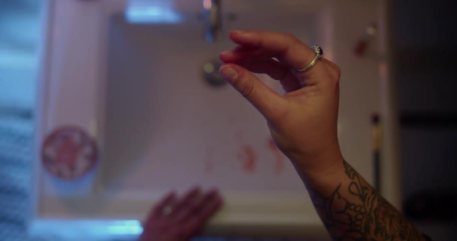 Woman looks at blood on her fingers as the blood drips into the sink