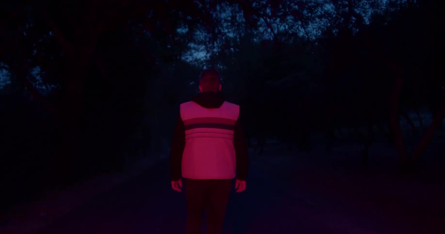 Man wearing vest walks down center of road at night