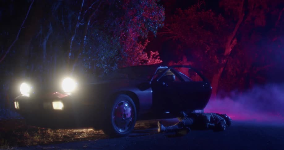 A body is laying outside of the car at night
