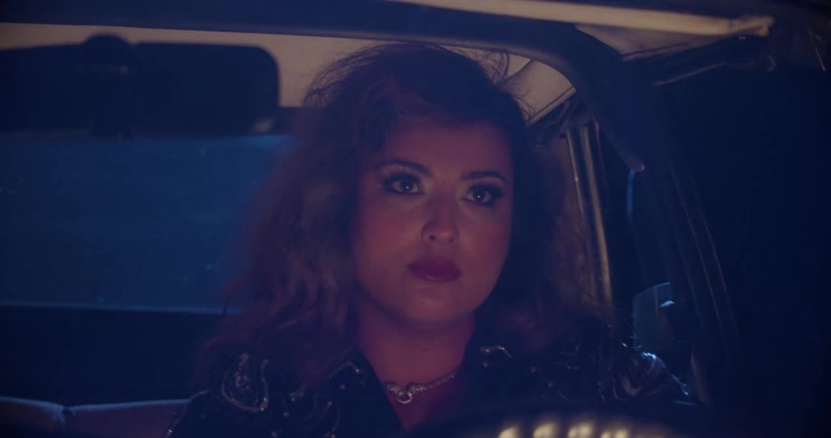 Woman driving in car stares wide eyed and open mouthed into rear view mirror