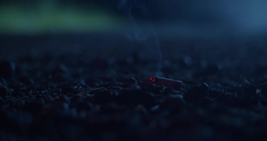 Smoke rises from burning cigarette laying on ground as nearby vehicle drives away