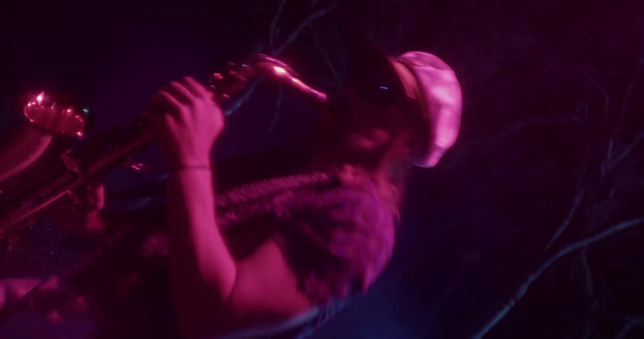 A man with a hat playing a saxophone surrounded by smoke with trees in the background