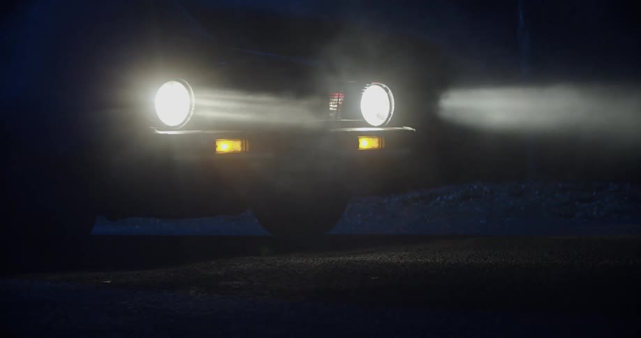 Car travels through the mist at night with its headlights and fog lights on