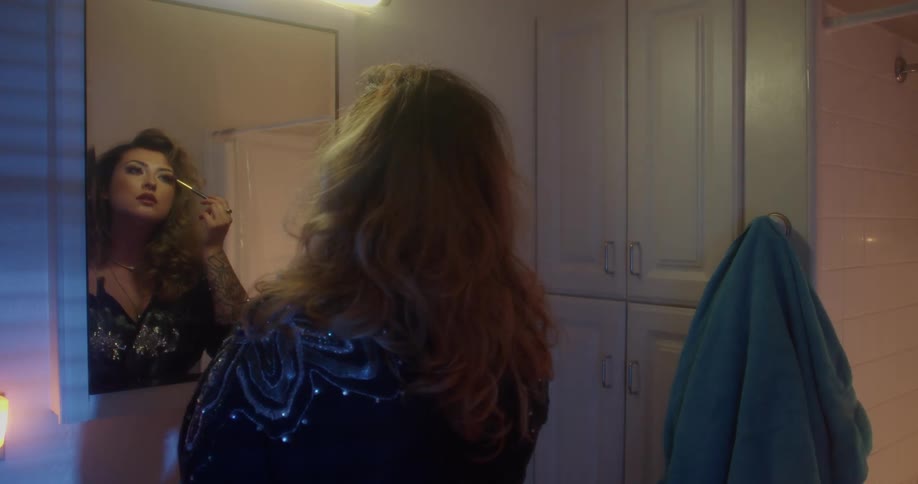 Woman stands in front of mirror putting on makeup as colored lights blink nearby