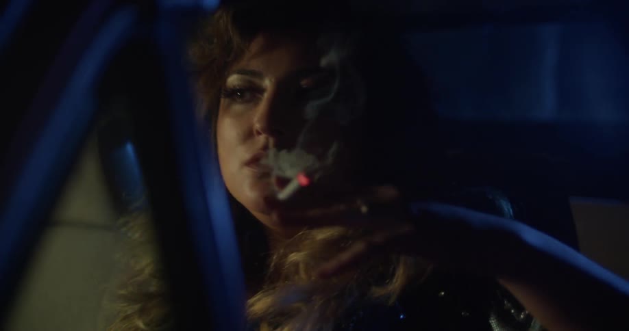 A woman sitting in a vehicle smoking a cigarette and blowing smoke