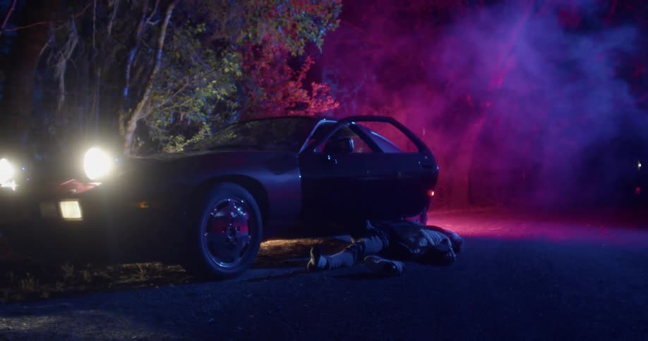 Dead body lays on the road next to a car in the forest