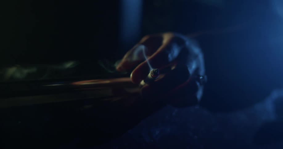 Smoke rises from a cigarette in a persons hand before they lift it up