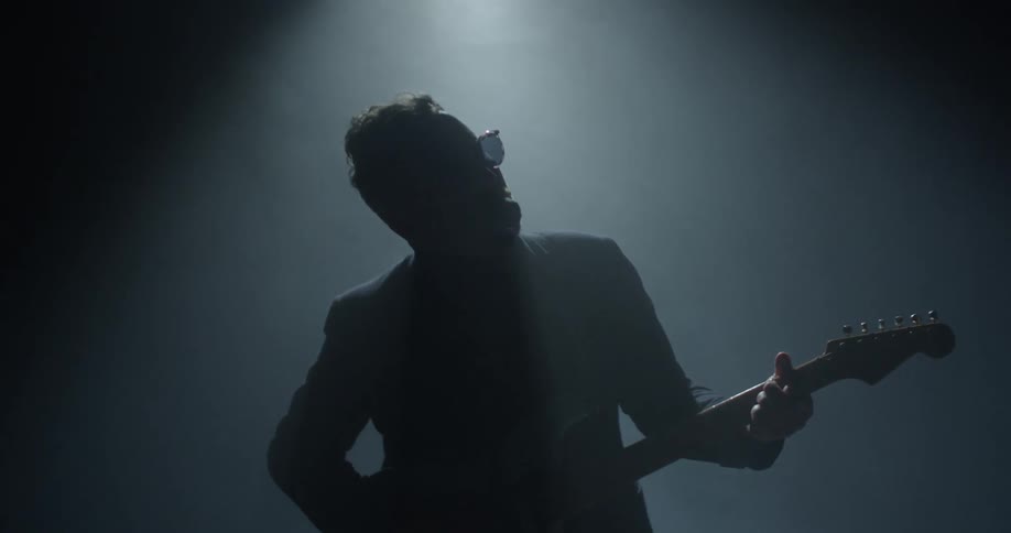 Man wearing glasses plays the guitar and sings into a microphone