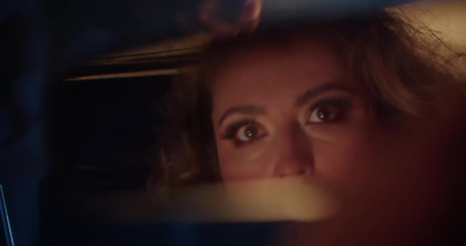 Woman looks fearful while looking in the rearview mirror in a car