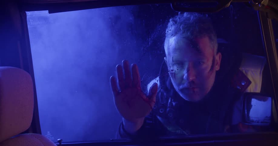 A man with a bloody hand touching a car window with a woman in the car