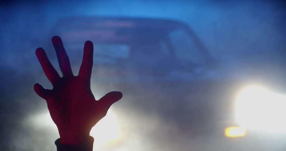 A vehicle with headlights and smoke with a persons hand in the foreground
